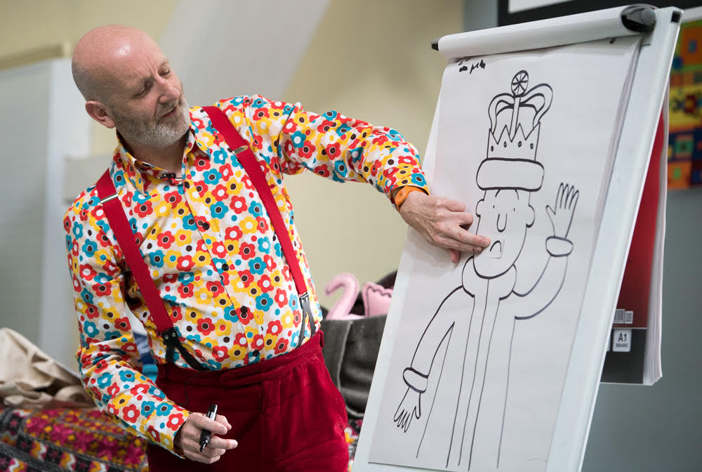 A man in a brightly-coloured shirt draws a cartoon of a king.